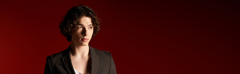 Obraz premium Young man with curly hair showcases stylish black attire in vibrant studio background