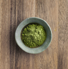 Kale powder in ceramic bowl on a wooden background, top view