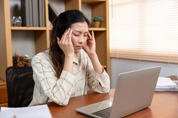 Asian woman sitting at desk working remotely with laptop, stressed and exhausted, closing eyes...