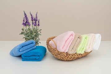A basket of towels is displayed on a table with a vase of purple flowers in the