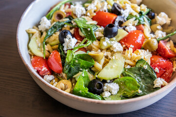  healthy orzo salad served in a bowl, made with fresh vegetables, black olives, and crumbled feta...