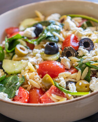  healthy orzo salad served in a bowl, made with fresh vegetables, black olives, and crumbled feta cheese close up