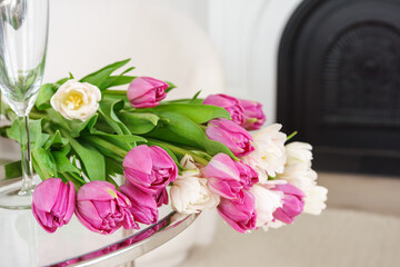 Vibrant bouquet or fresh pink and white tulips is elegantly arranged on glass table in white living room background. Home decor. Festive atmosphere, holiday, celebration event.
