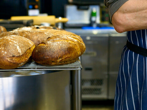 Loaves of sour dough artisan bread on rack in bakery with baker