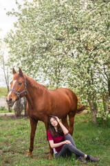 A female horse owner and a thoroughbred mare on the background of a blooming apple tree
