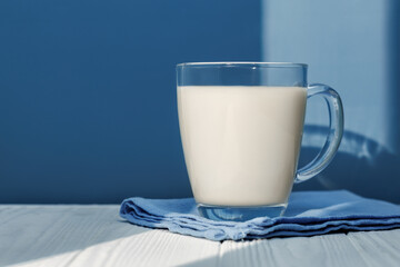 Sunlight illuminating glass milk resting on blue napkin on white wooden table with blue background, creating cozy scene
