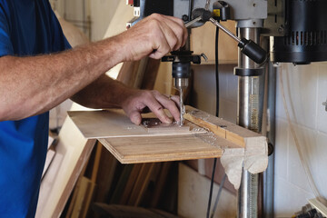 Carpenter using vertical drilling machine in woodwork workshop