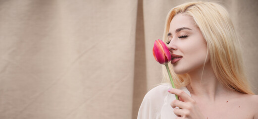 Lips closeup Portrait of a beautiful blonde girl with a pink tulip on a beige background. Lip...