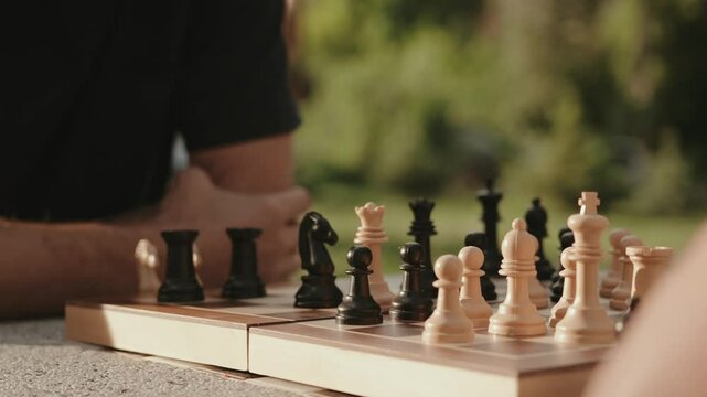 A close up shot of a chess board outdoors with two people about to make their next strategic move on a sunny day. 