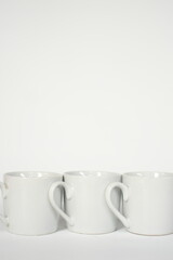 White ceramic mugs arranged in a row showcasing their elegant heart shaped handles against on white background