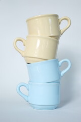 Stack of beige and blue ceramic mugs on white background. Reusable coffee cups stacked in a balanced manner