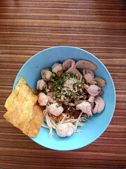 Noodles with pork and vegetables in blue bowl on wooden table