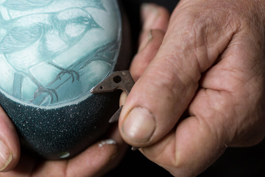 Closeup of man's hands engraving image on emu egg shell