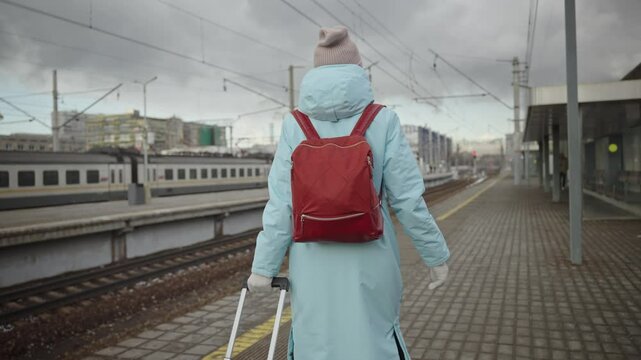 A woman in a winter coat walks along a train platform with her suitcase on a gloomy, snowless day. Captures the essence of Eastern Europe's urban transport infrastructure during the chilly off-season.