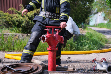 A firefighter in full protective gear operates a red fire hydrant on a sunny day.