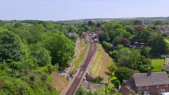 Slow motion drone shot of Corfe Castle railway station surrounded by green countryside and village
