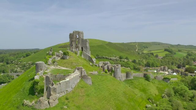 Drone image capturing Corfe Castle&rsquo;s ancient ruins, rolling green hills, and nearby village activity in Dorset, England on a bright and clear summer day