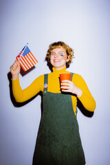 A young woman beams with happiness as she proudly waves a small American flag while holding a red...