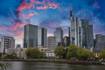 Modern skyline of Frankfurt, Germany, featuring the Commerzbank Tower, tree lined waterfront, and a mix of contemporary and historic architecture.