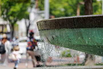 Water elegantly cascades over the edge of a stone fountain, capturing sunlight in sparkling...