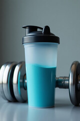 Protein Shaker. A transparent protein shaker bottle half-filled with protein powder next to the dumbbells.
