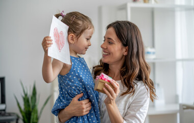 A little girl gives her mom a heart-shaped drawing and a gift box for Mother's Day.