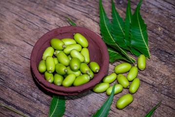 Fresh Neem fruit on wooden bowl and neem green leaf on rustic wooden background.