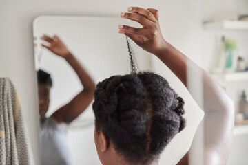 Young African woman examining her hair in a bathroom mirror