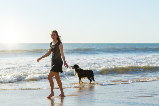 Young woman walking along beach with border-collie dog - Powered by Adobe