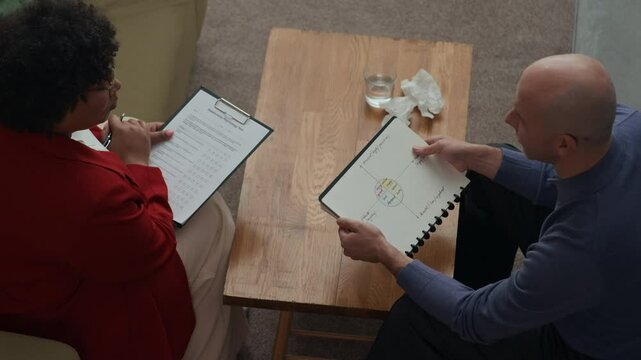 View from above of female African American psychologist analyzing mans mental health using form and emotion chart