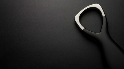 A sleek black and silver tongue scraper on a minimalist dark background.