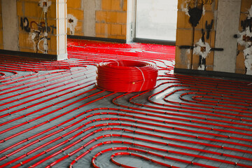 Installing underfloor heating system with red pipes in a building under construction