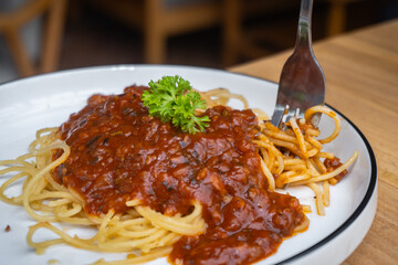 Delicious spaghetti bolognese on white plate on cafe table. Pick up spaghetti using a fork.