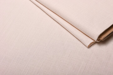 Flat lay of beige lightweight linen fabric on the table. The soft, natural texture embodies craftsmanship, tailoring, and timeless textile artistry.