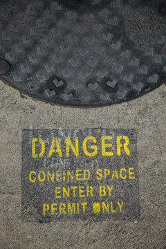 Danger confined space enter by permit only sign in car park beside man hole
