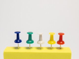 Colorful Push Pins in a Row on a Yellow Block Against a White Background