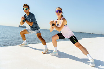 Dynamic duo engages in energetic workout by the waterfront on a sunny day, showcasing fitness and motivation