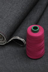 Pink sewing thread rest atop of a grey jeans fabric, representing craftsmanship, fashion tailoring, and precision in garment-making.