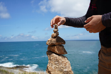A man and a woman are carefully stacking rocks in an artistic manner near the ocean.
