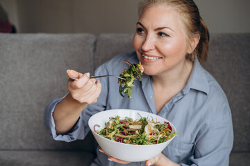 Smiling woman eats a salad with arugula and vegetables, healthy eating at home	
