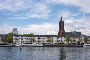 Fototapeta premium View of Frankfurt, Germany, featuring the Gothic style Frankfurt Cathedral, the Main River with moored boats, and modern high rise buildings in the background.