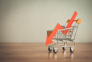 Shopping trolley with red chart falling down on wooden table white wall background copy space. Economic recession crisis, core retail sales decrease, inflation or goods price up concept.
