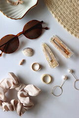 Sunglasses, straw hat, shells and jewelry in neutral colors. Seasonal summer accessories on white background. Flat lay.