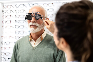 Professional ophthalmologist or optician testing senior man eyesight and diopter in eye clinic.