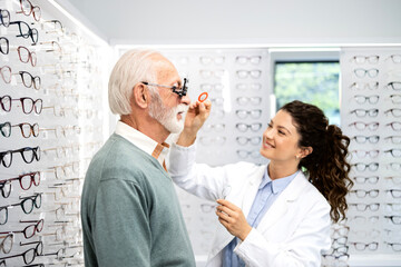 Obraz premium Experienced female optician or ophthalmologist examining senior patient and checking diopter and eyesight.