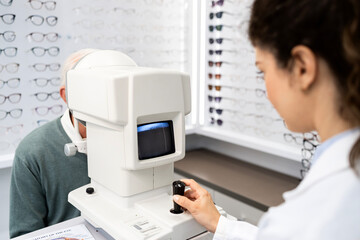 Professional ophthalmologist testing patient eyesight and diopter using auto refractor optics instrument.