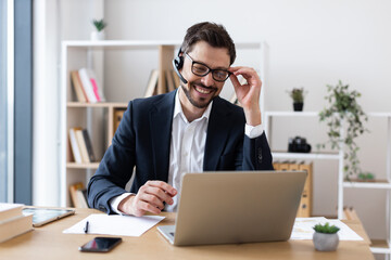 Smiling adult male wearing suit using laptop during business communication in office setting.