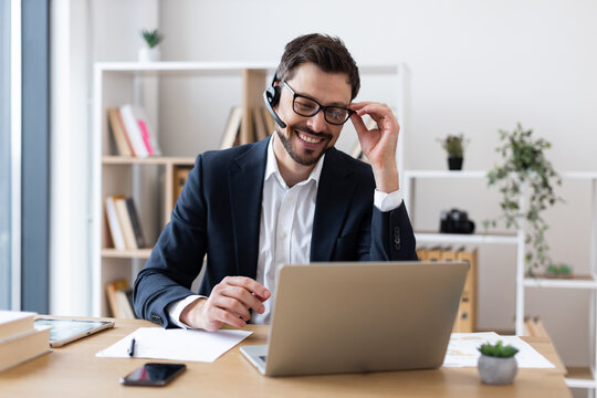 Smiling adult male wearing suit using laptop during business communication in office setting.