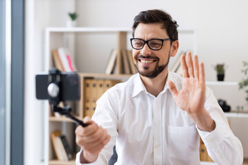 Middle-aged man recording video call with smartphone indoors expressing happiness and engagement....