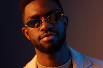 Stylish young African man with sunglasses against a vibrant gradient background, exuding confidence and modern fashion in a contemporary portrait